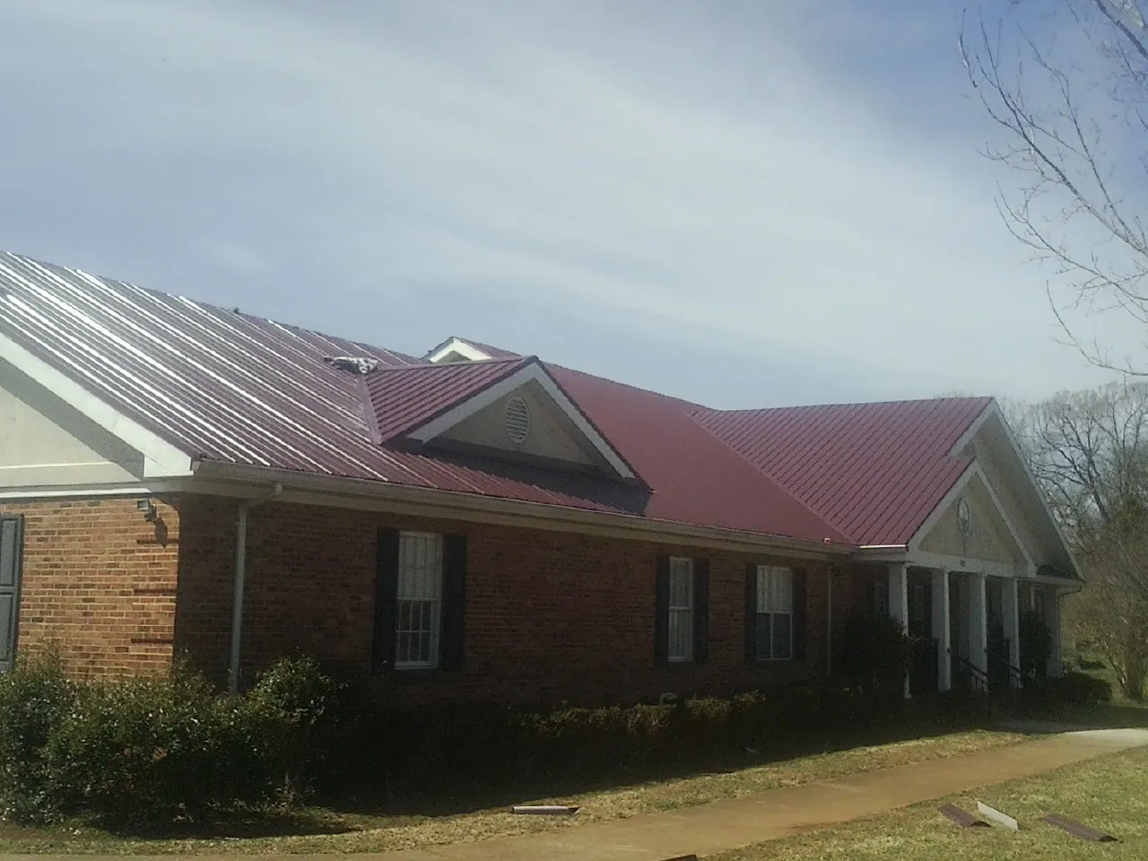 Red metal roof with gabled entries on a long brick building, from a Hail Damage Roof Repair job in Goodell