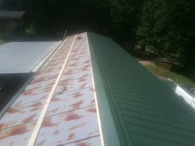 Old rusted panels beside newly installed green metal roofing — Wind Damage Roof Repair by Roofing Brothers in Goodell