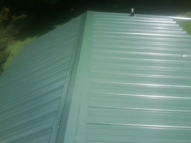 New green metal panels meeting at the ridge of a roof — Flat Roof Repair work by our crew in Goodell