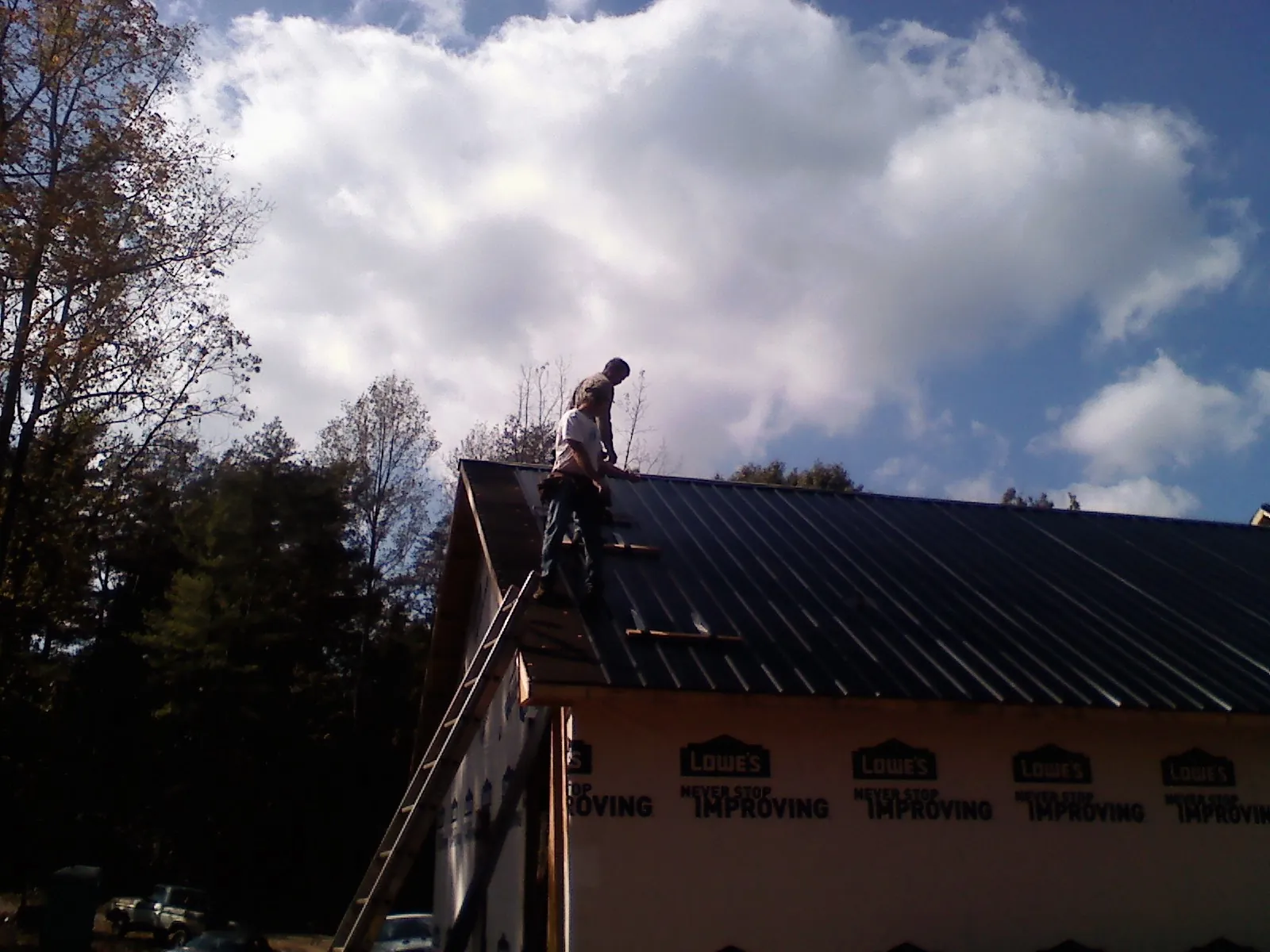 Roofer fastening dark metal panels high against a cloudy sky, from a Roof Inspection job in Goodell
