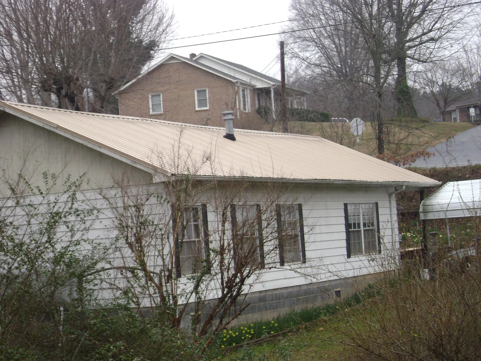Tan metal roof on a white sided house set into a hillside — Commercial Roofing by Roofing Brothers in Goodell