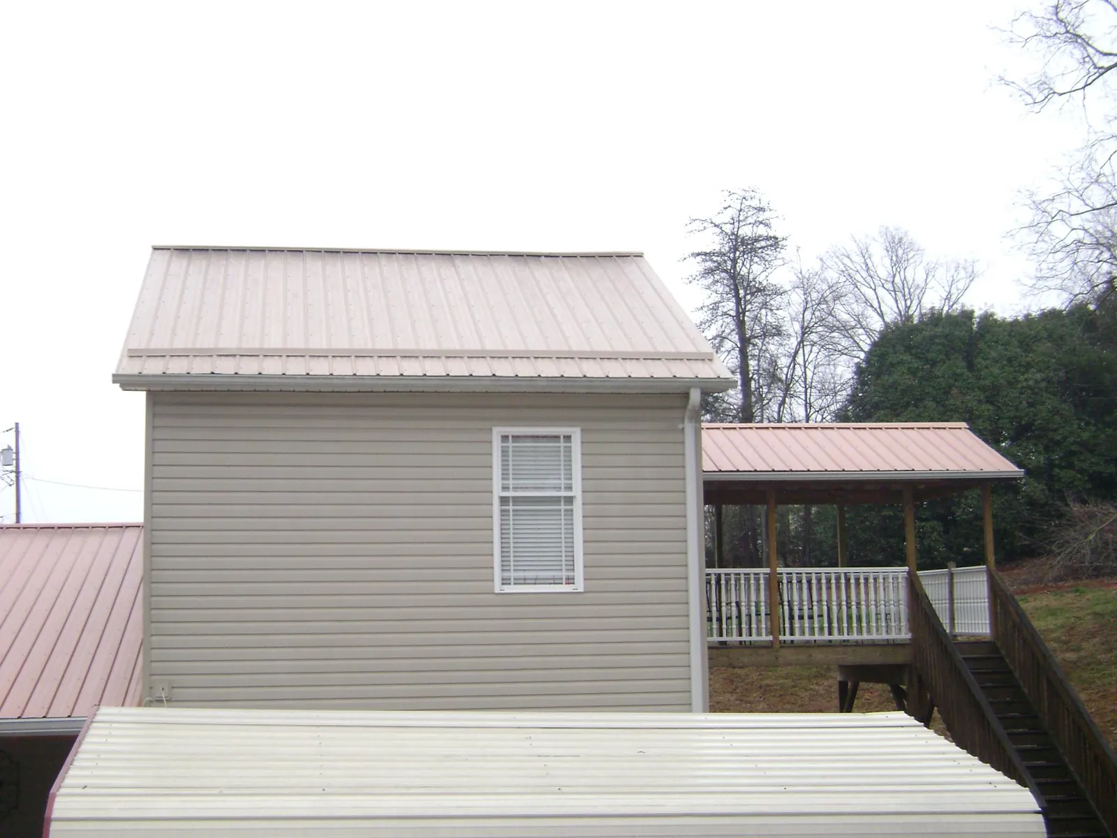 Tan metal roofs on a two story addition and attached porch, from a Roof Replacement job in Goodell