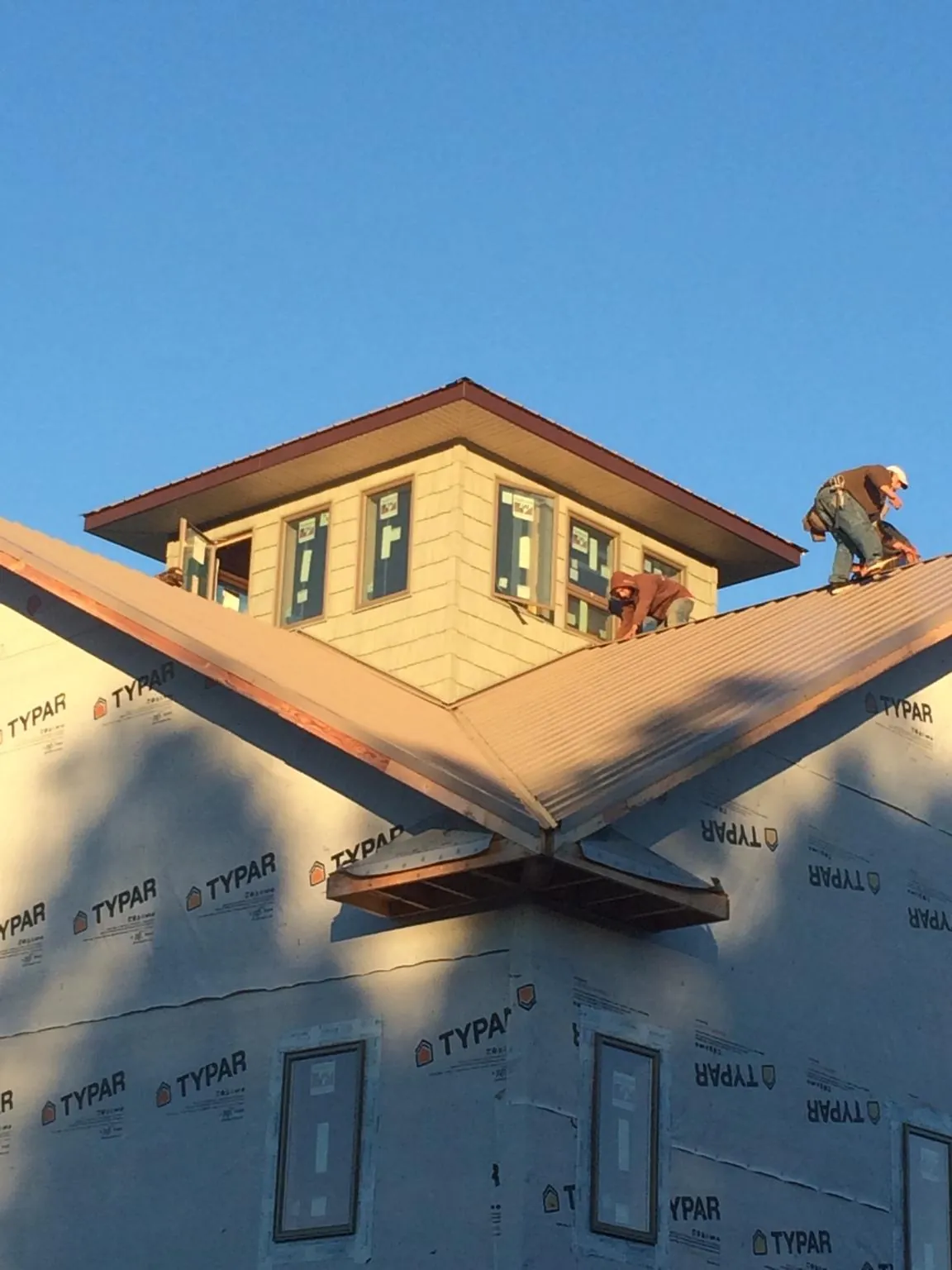 Roofers working around a rooftop cupola on a new metal roof at sunset — Roof Waterproofing in Goodell by Roofing Brothers